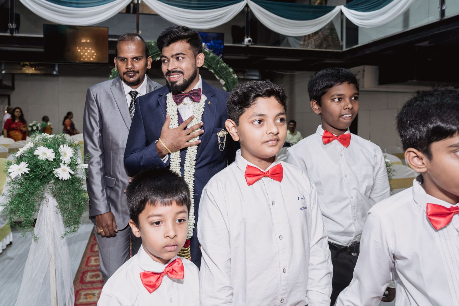 Wedding party members pose together with young ring bearers in matching red bow ties.