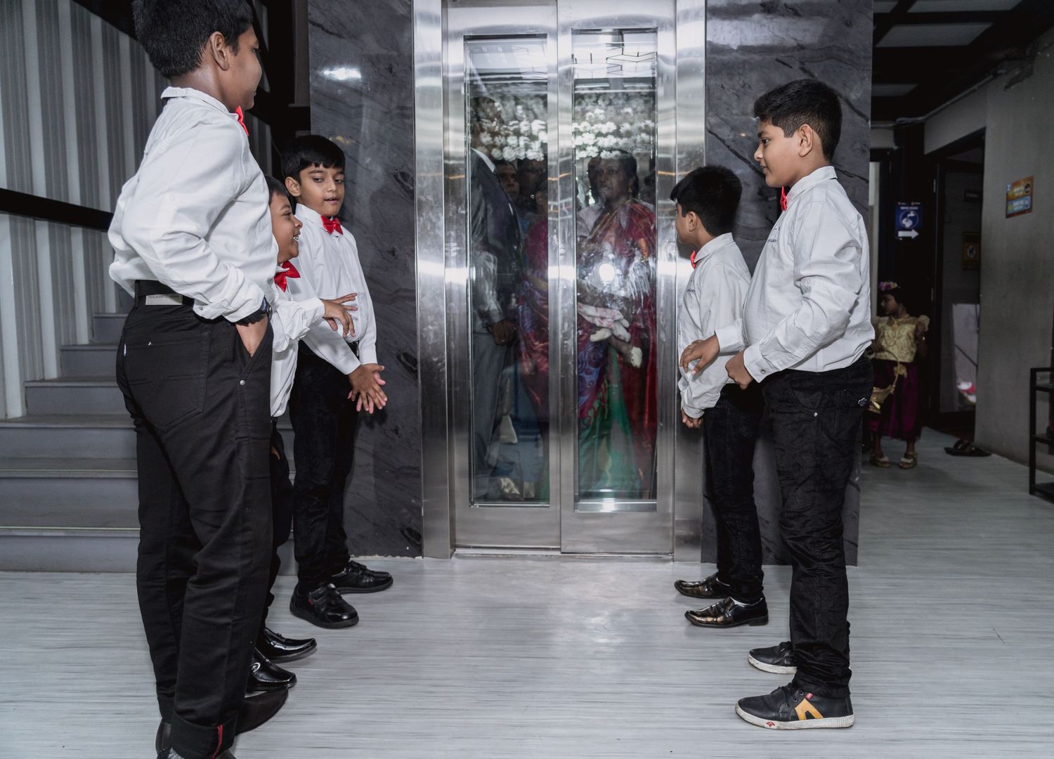 A group of formally dressed young attendants gather near an elevator.