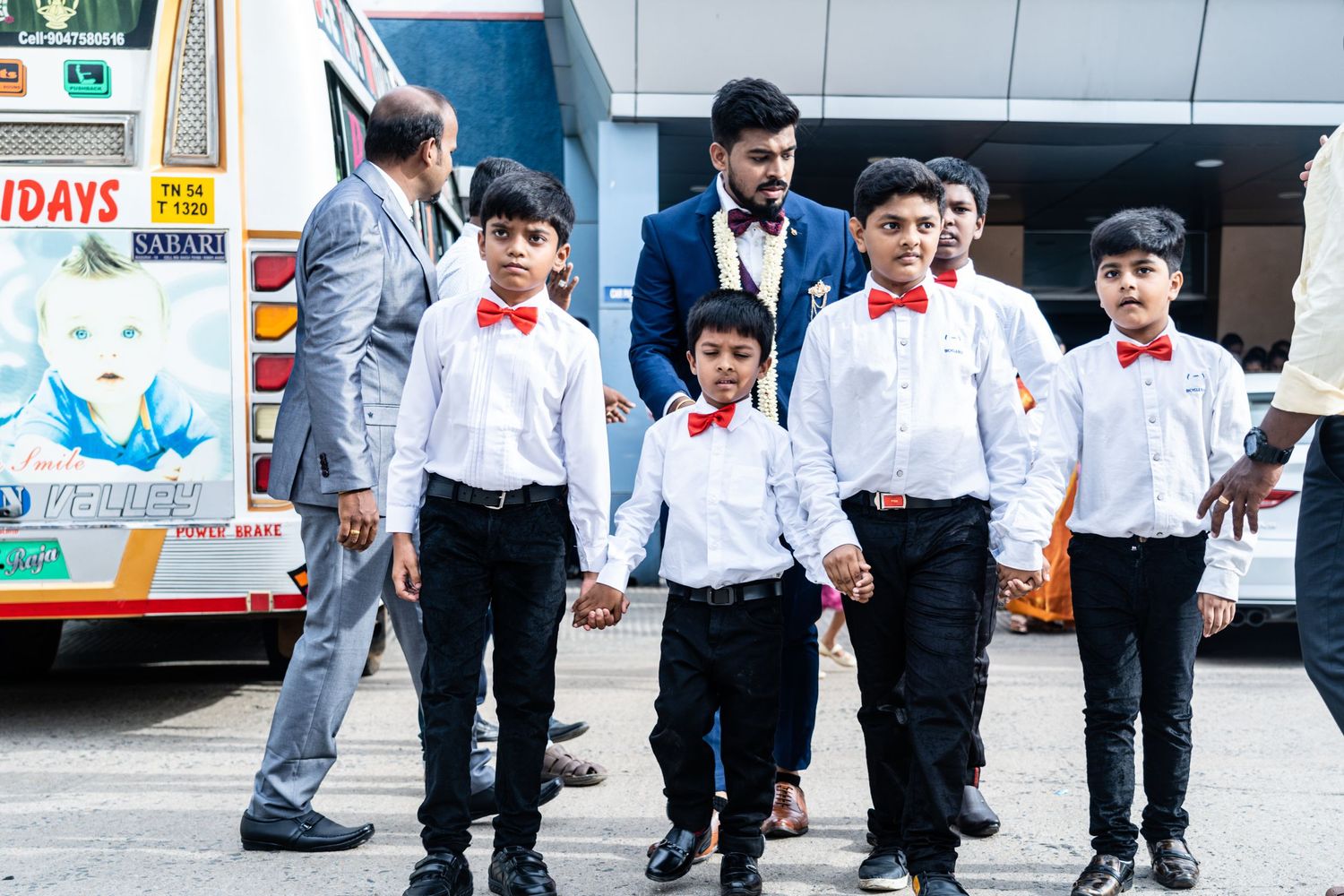 Young ring bearers in matching formal attire with red bow ties line up outside.