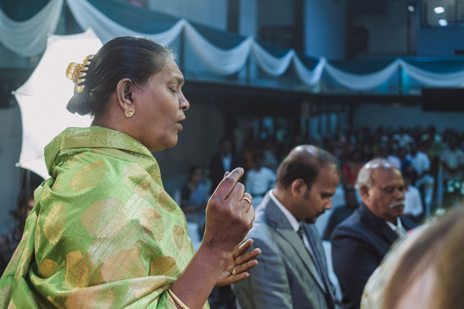 Guest in green and gold sari observing wedding ceremony proceedings.