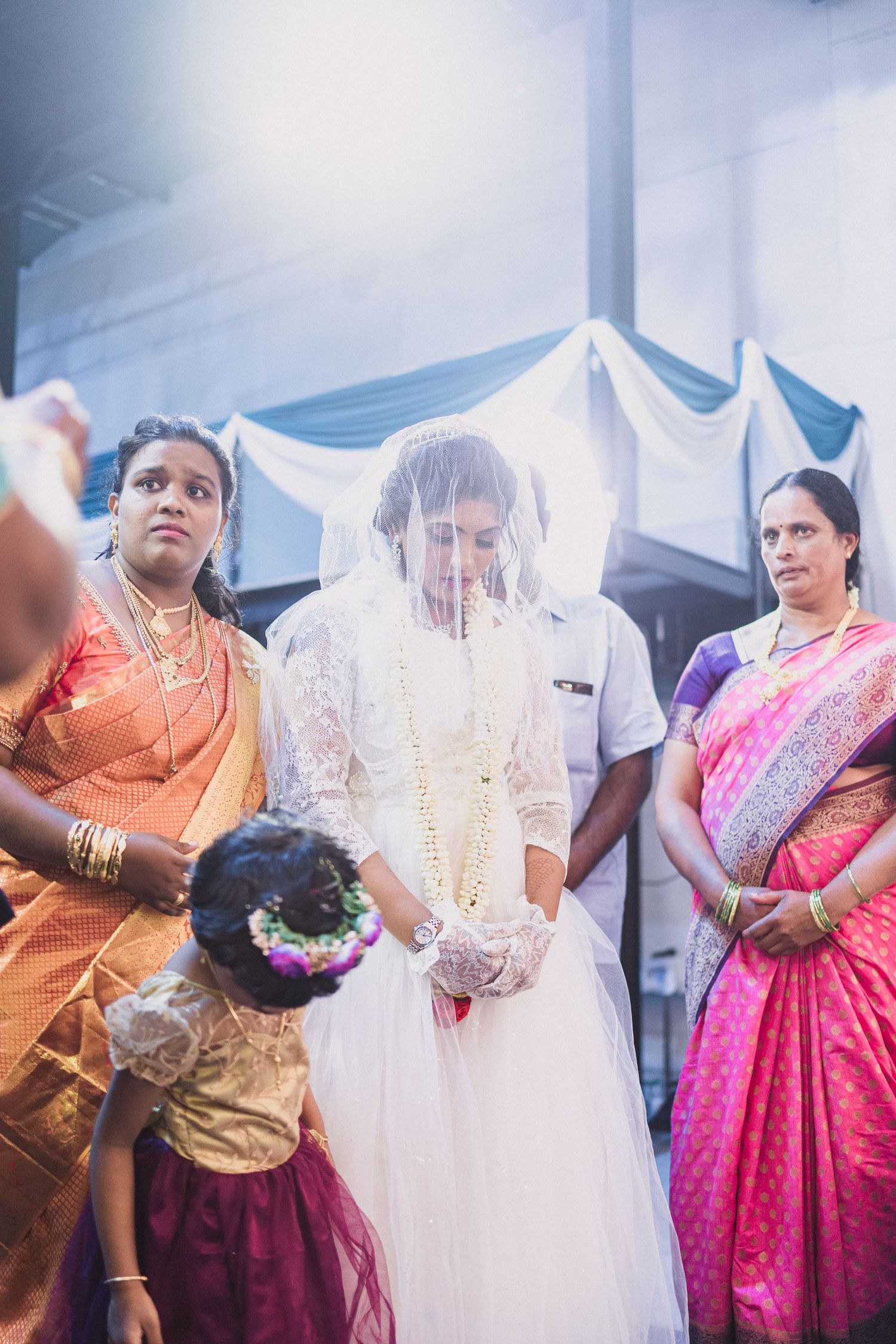 Wedding ceremony with attendees wearing traditional Indian saris in vibrant orange and pink.