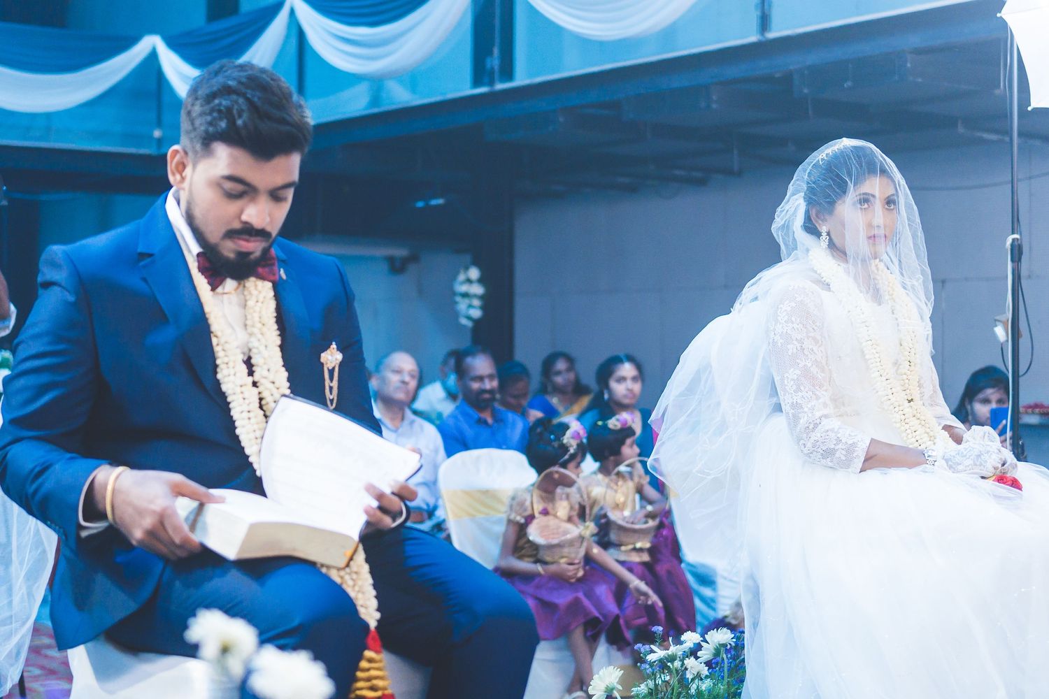 Wedding ceremony participant in blue suit reading from a book during the service.