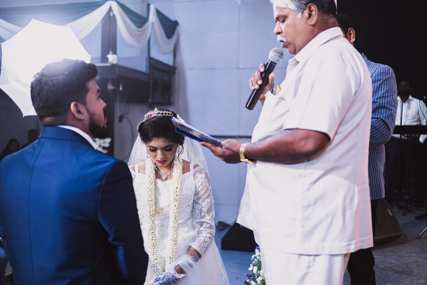 Wedding officiant speaks into microphone as couple participates in ceremony.