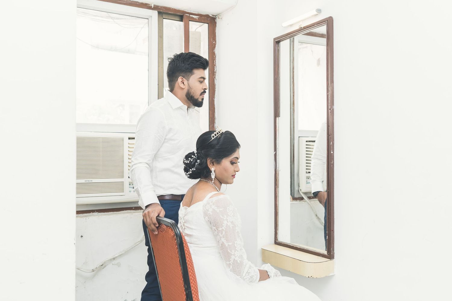 A couple getting ready in a bright white interior room with mirrors during wedding preparations.