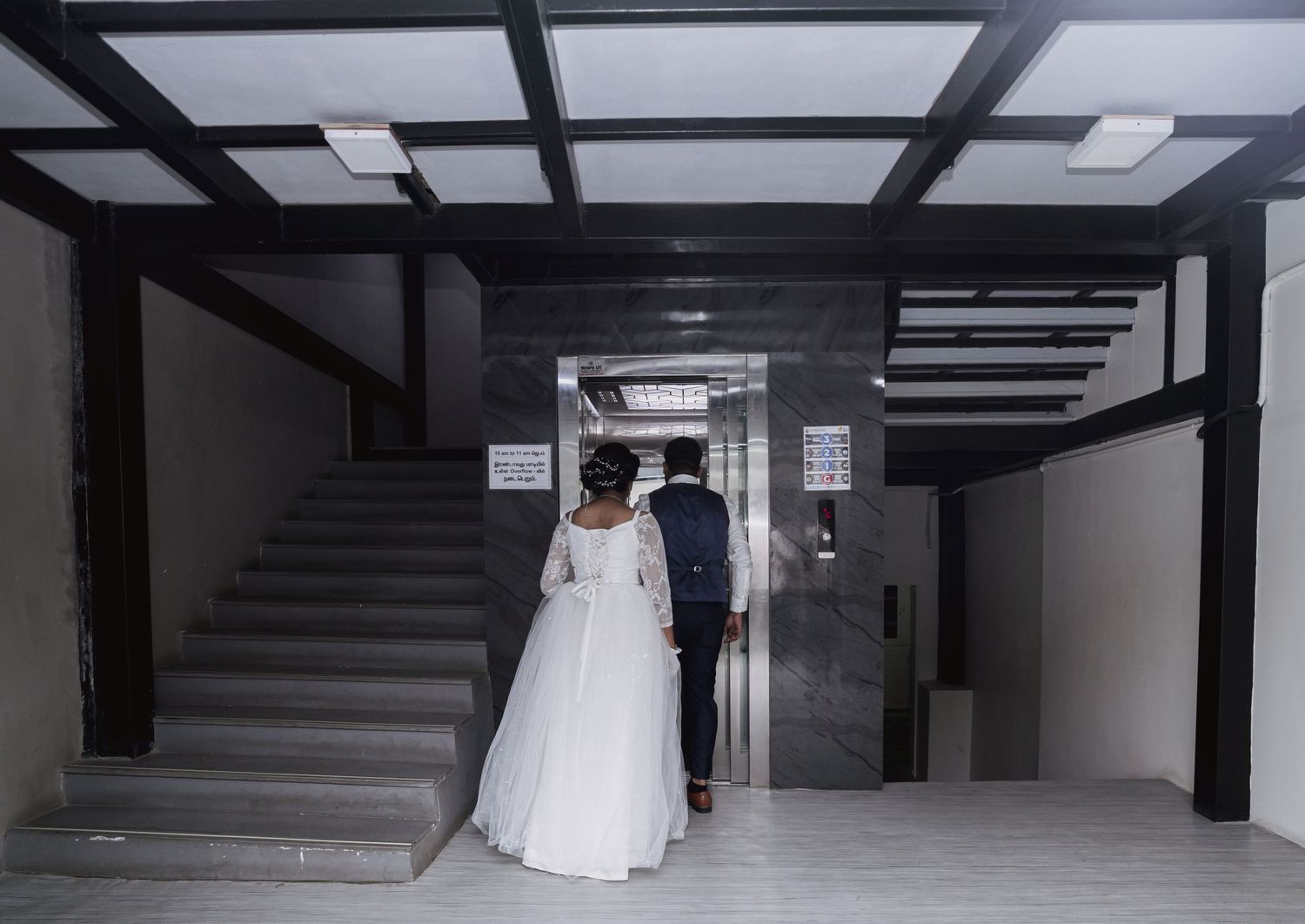 A bride and groom walk up a modern stairwell together on their wedding day.