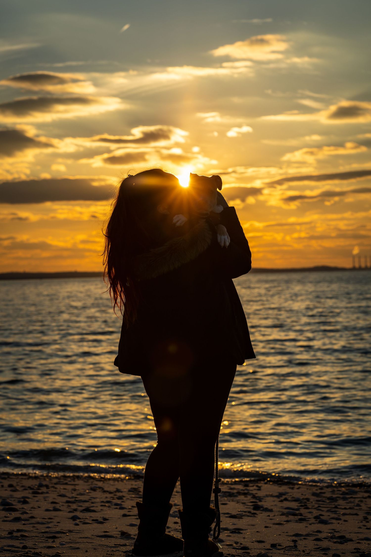 Silhouette of a person standing on beach during dramatic sunset over water.