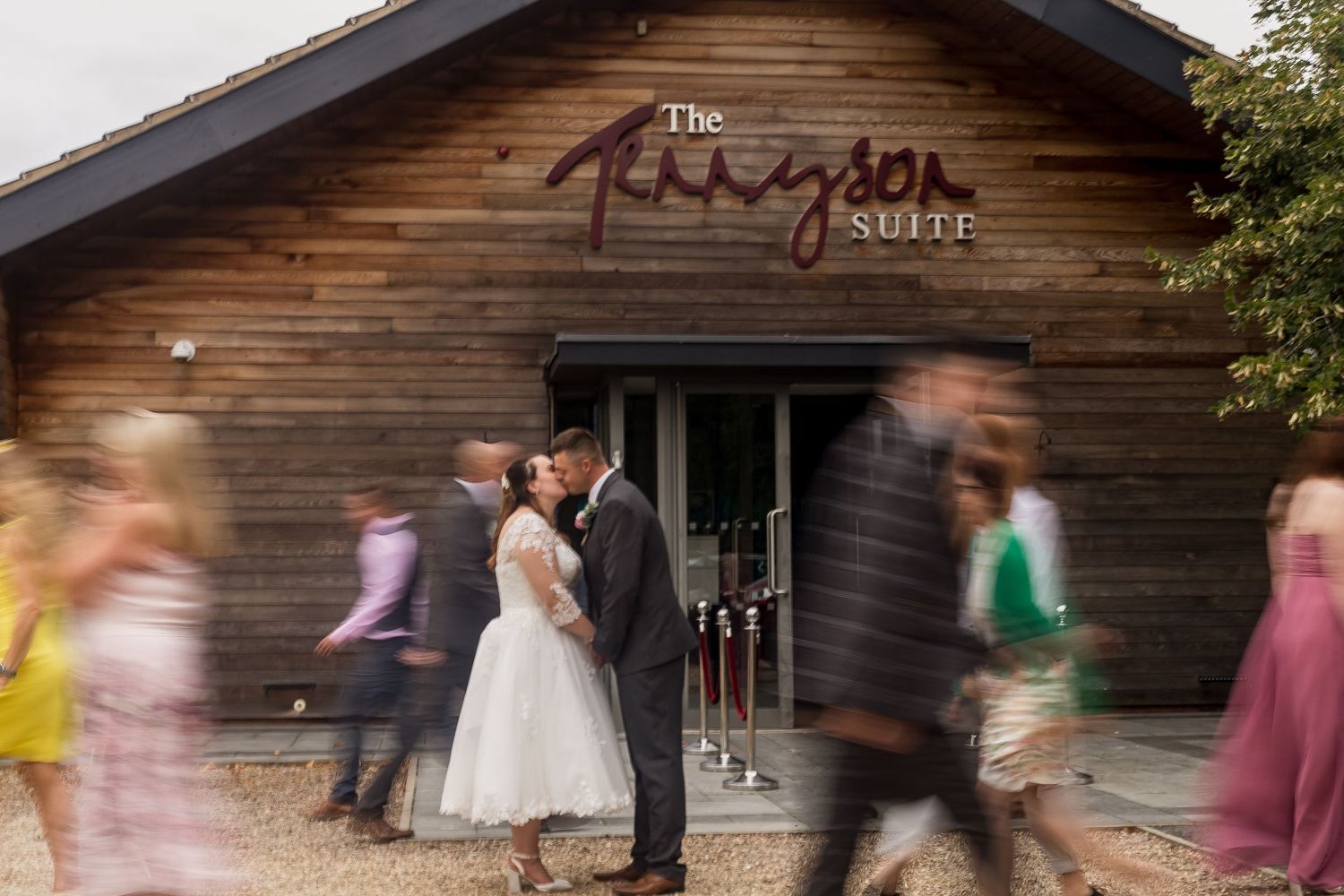 Motion blur photo of wedding party dancing in front of rustic wooden building.