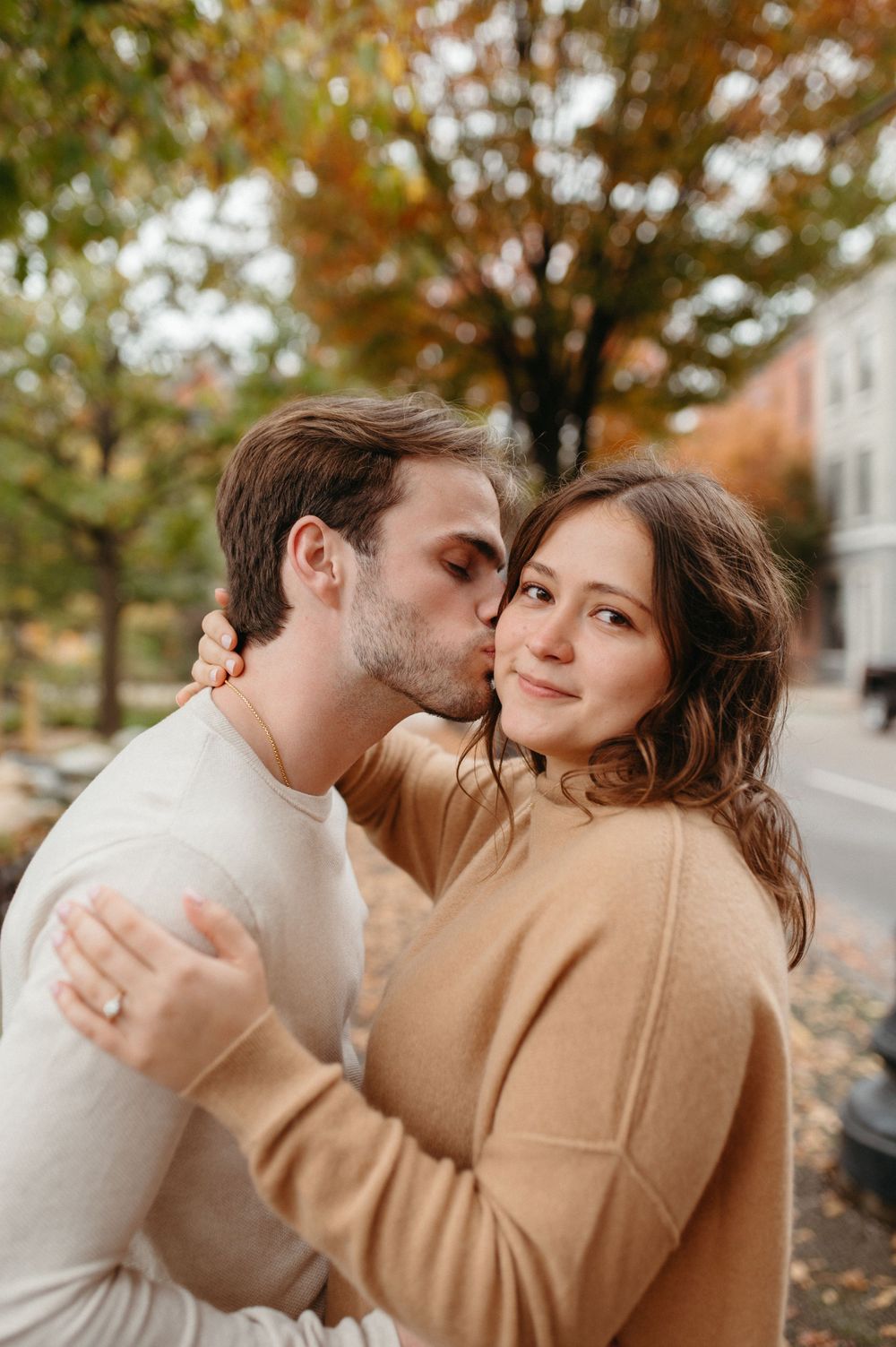 Couple sharing an intimate moment on a tree-lined street during fall season.