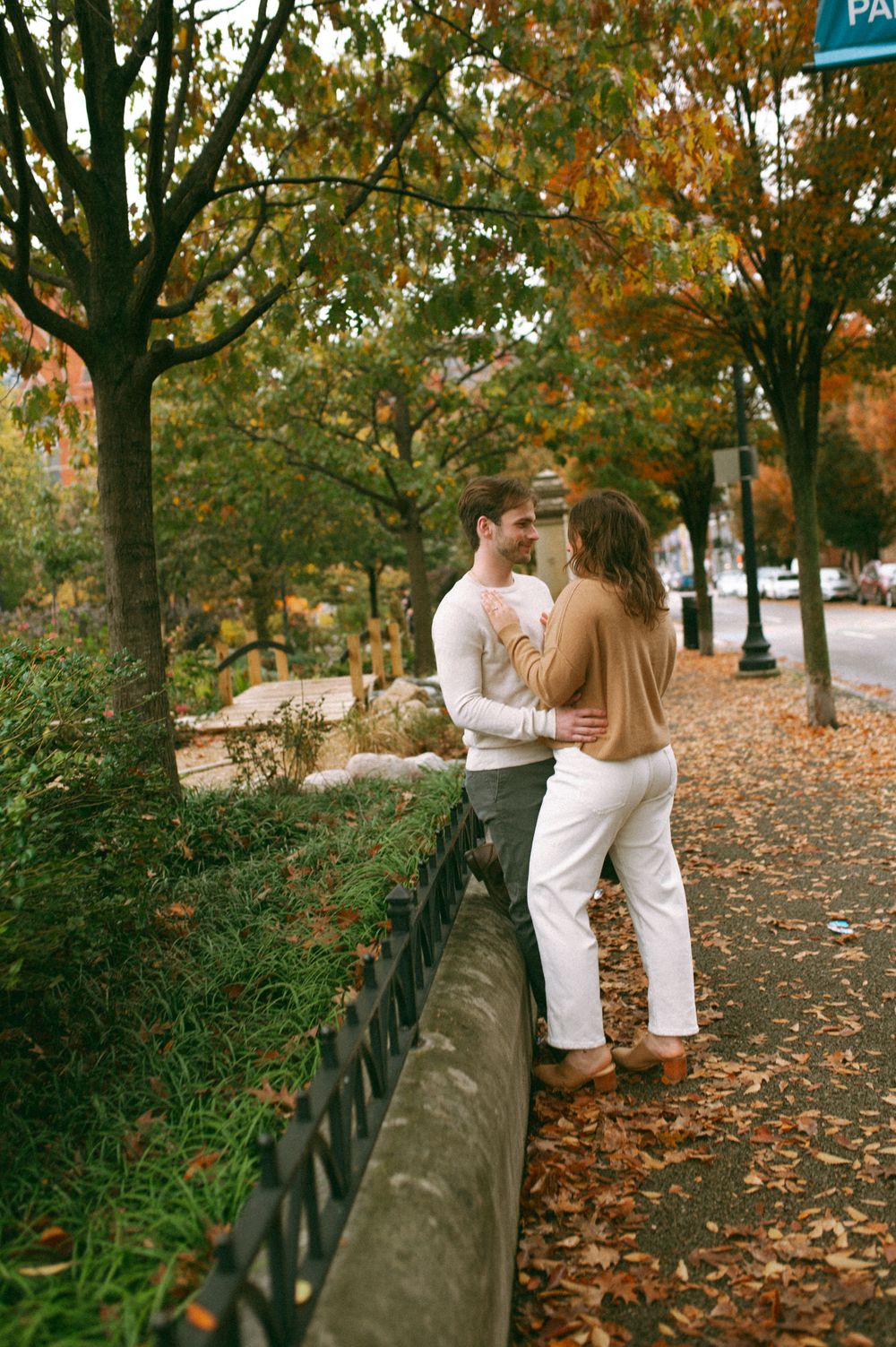 A couple shares an intimate moment along a leaf-covered pathway during autumn.