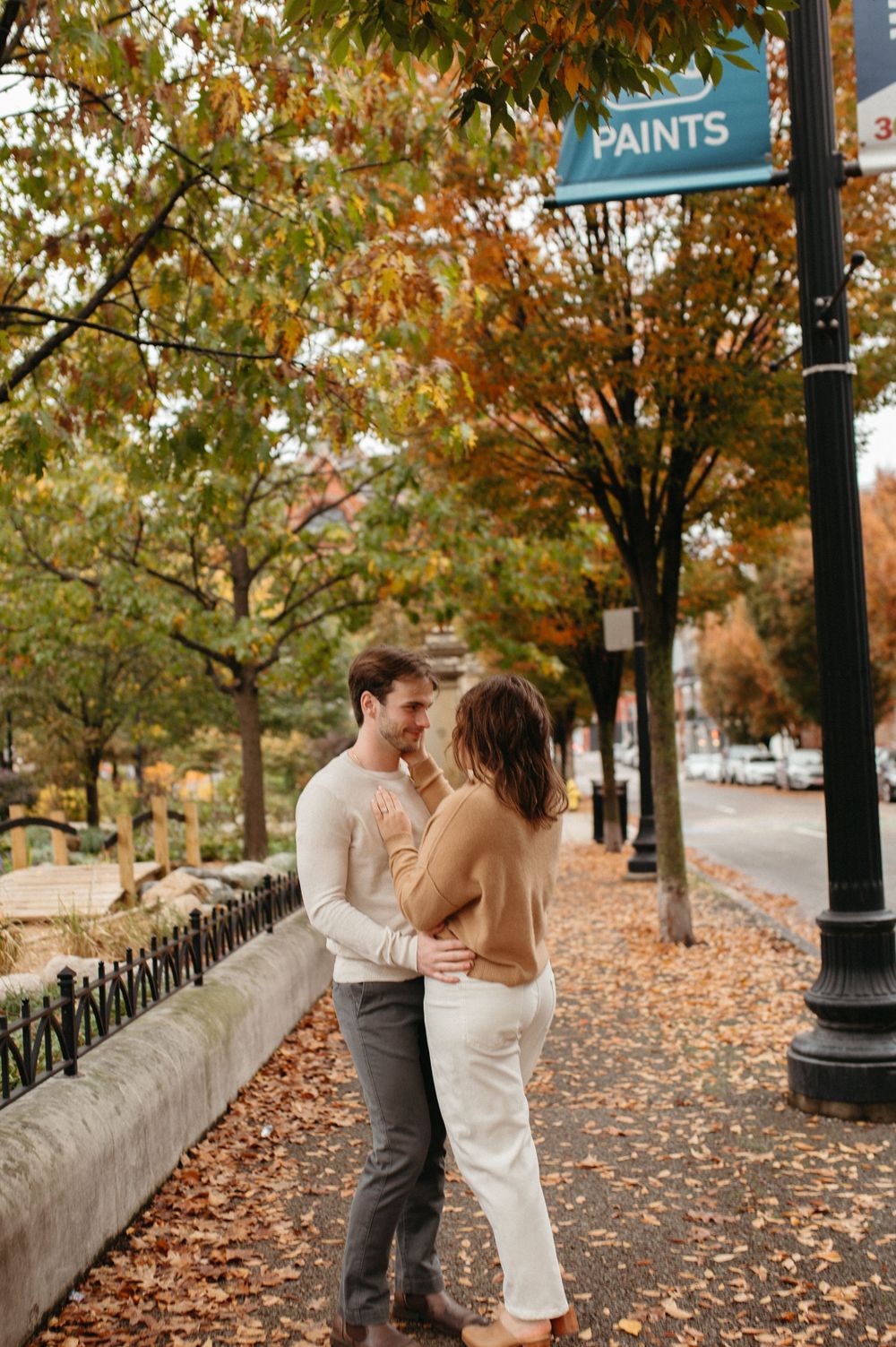 A romantic embrace on a city sidewalk decorated with autumn foliage and fallen leaves.