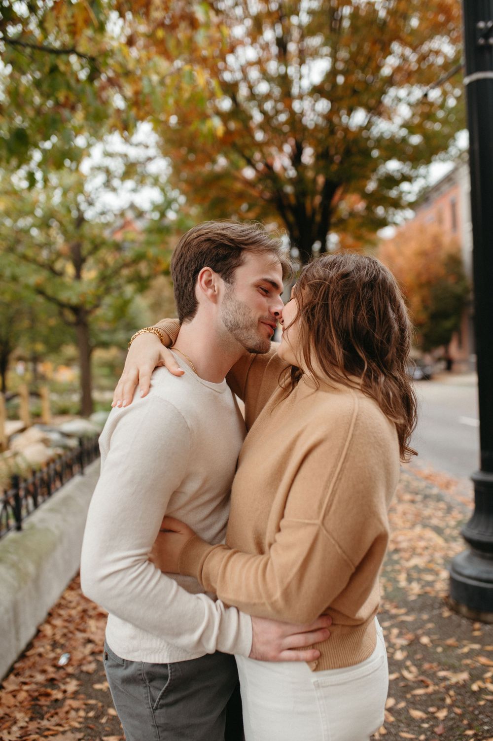 An intimate embrace between a couple on a fall day surrounded by golden autumn trees.