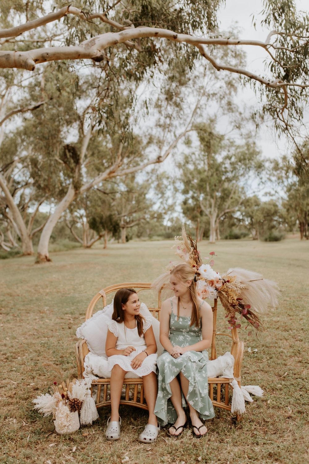 sisters sitting on a cane chair smiling at eachother