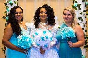 A bride in white and bridesmaids in turquoise dresses hold illuminated bouquets against a floral backdrop.