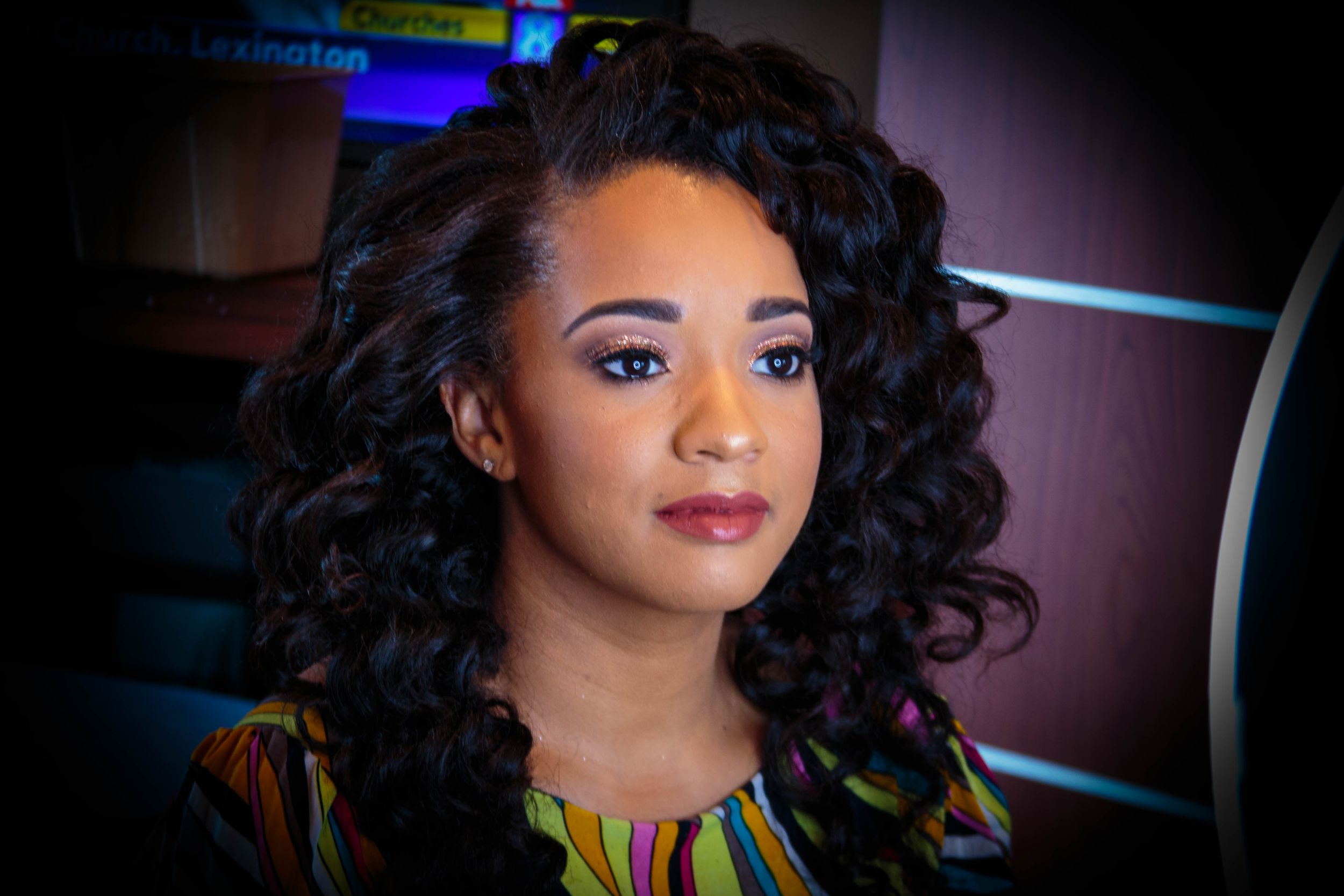 Close up portrait against dark background showing glamorous curled hairstyle and evening makeup.