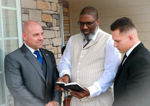 Three men review documents together on an outdoor porch.