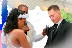 Wedding ceremony exchange of vows beneath white backdrop.