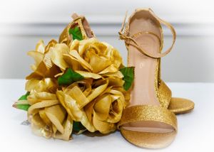 Gold roses arranged next to a beige sandal with sparkly straps.