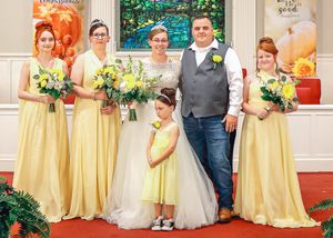 Wedding group photo with bridesmaids in yellow dresses and groomsmen in gray vests.