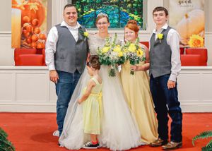 Wedding party in yellow bridesmaid dresses and gray vests posing for formal photo.