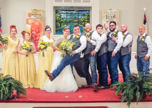 Fun wedding party photo with groomsmen striking playful poses on red carpet.
