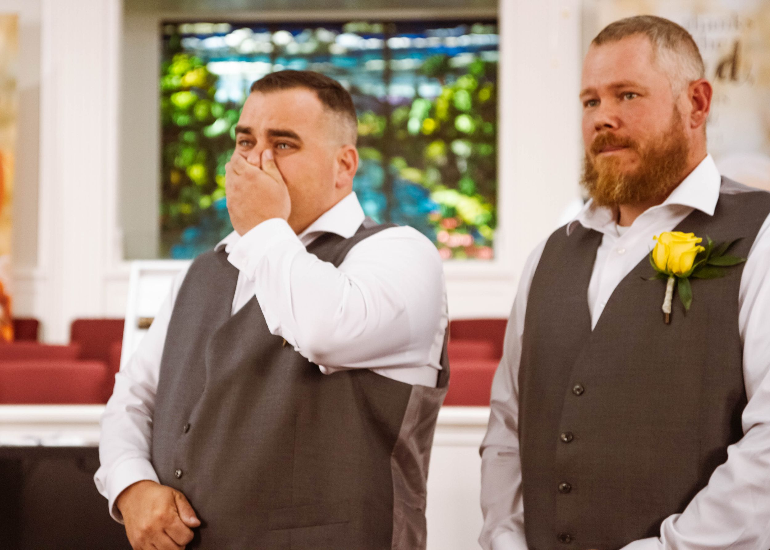 Emotional moment captured during wedding ceremony with two men in gray vests.