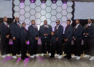 Groomsmen in dark suits posing together against geometric backdrop with purple lighting.