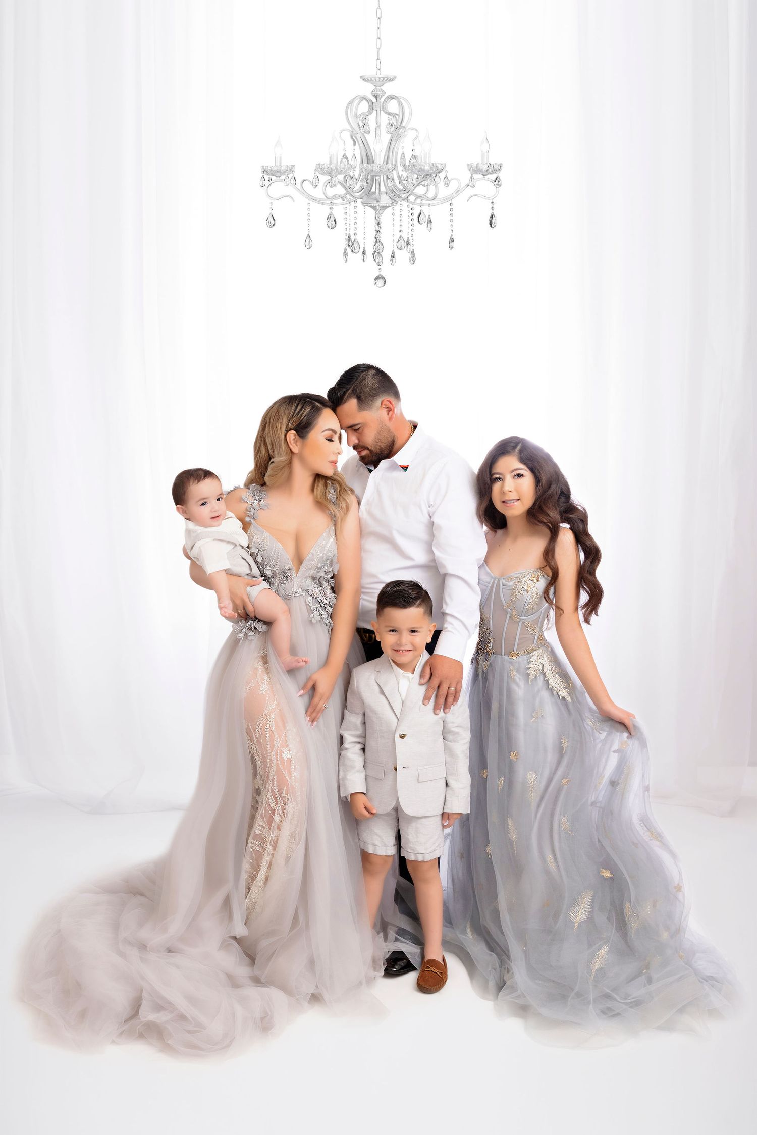 Family wearing coordinated gray formal gowns poses beneath crystal chandelier.
