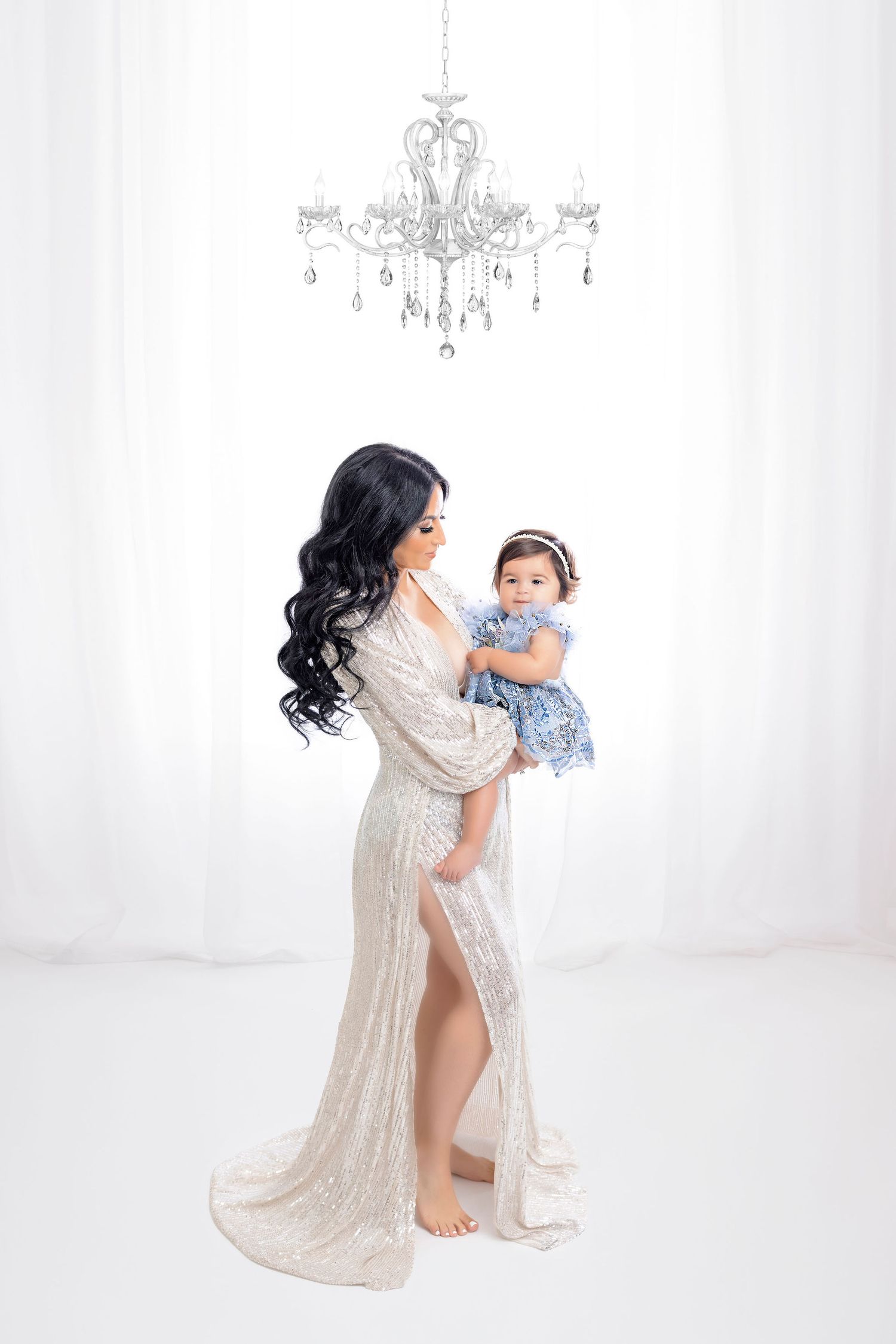 Glamorous studio portrait under a crystal chandelier with a shimmering silver gown against white.