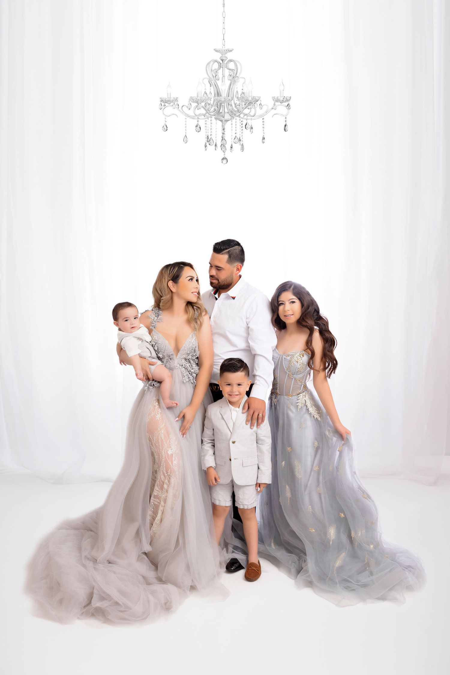 Glamorous family photo with flowing silver gowns under elegant chandelier.