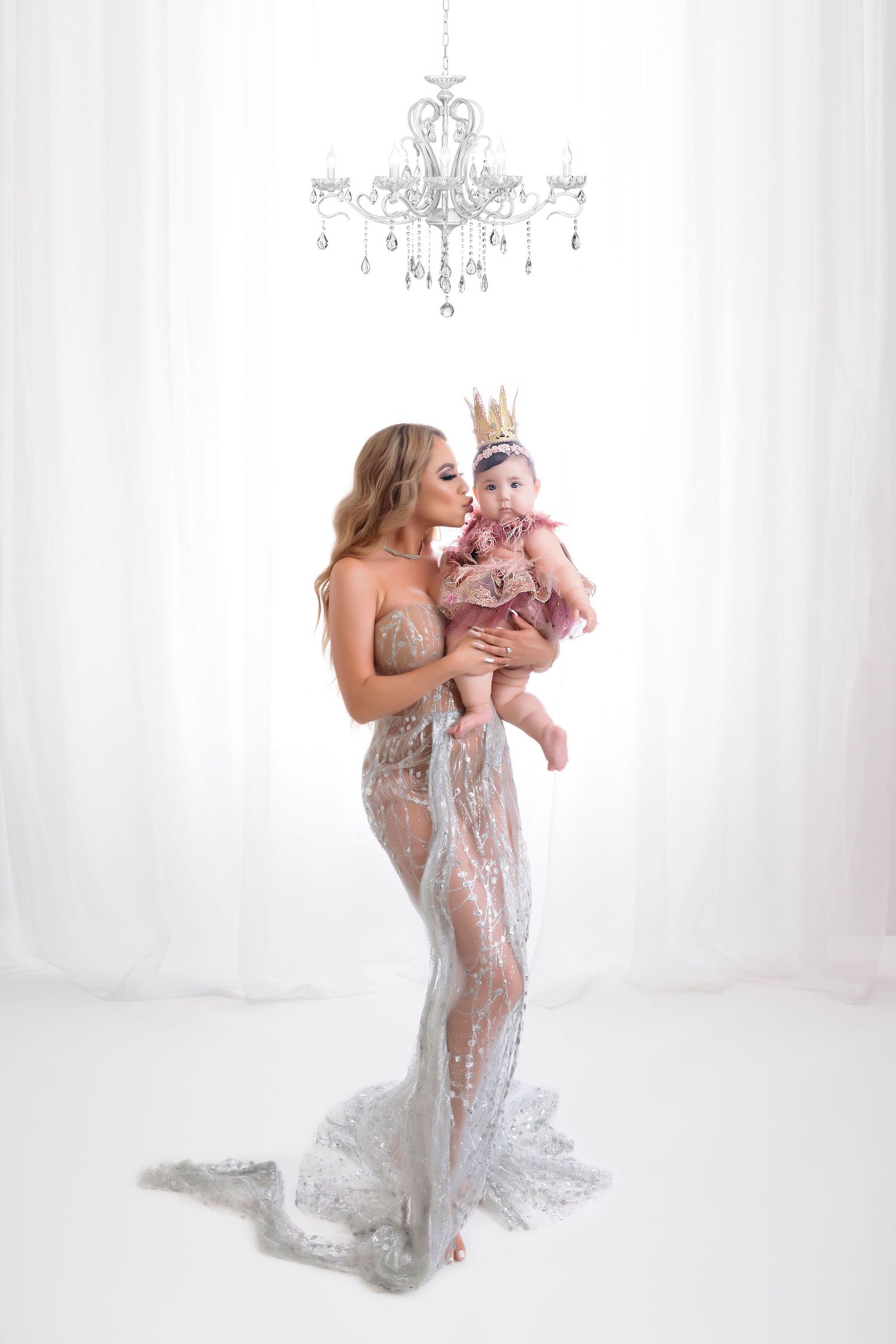 Dreamy studio portrait under a crystal chandelier featuring a lace gown and soft white backdrop.