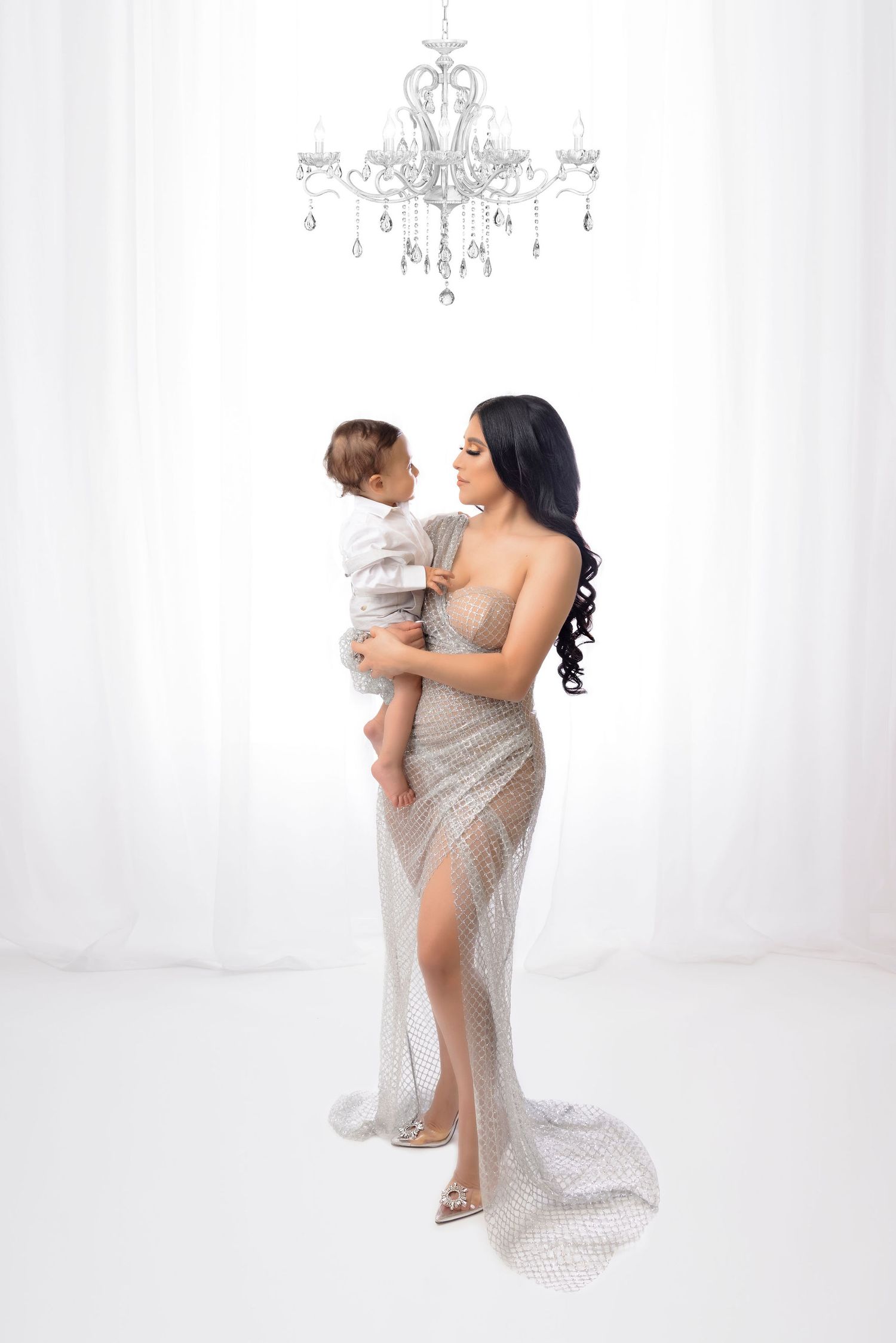 An elegant portrait with two people under a crystal chandelier, wearing a sparkly silver gown.