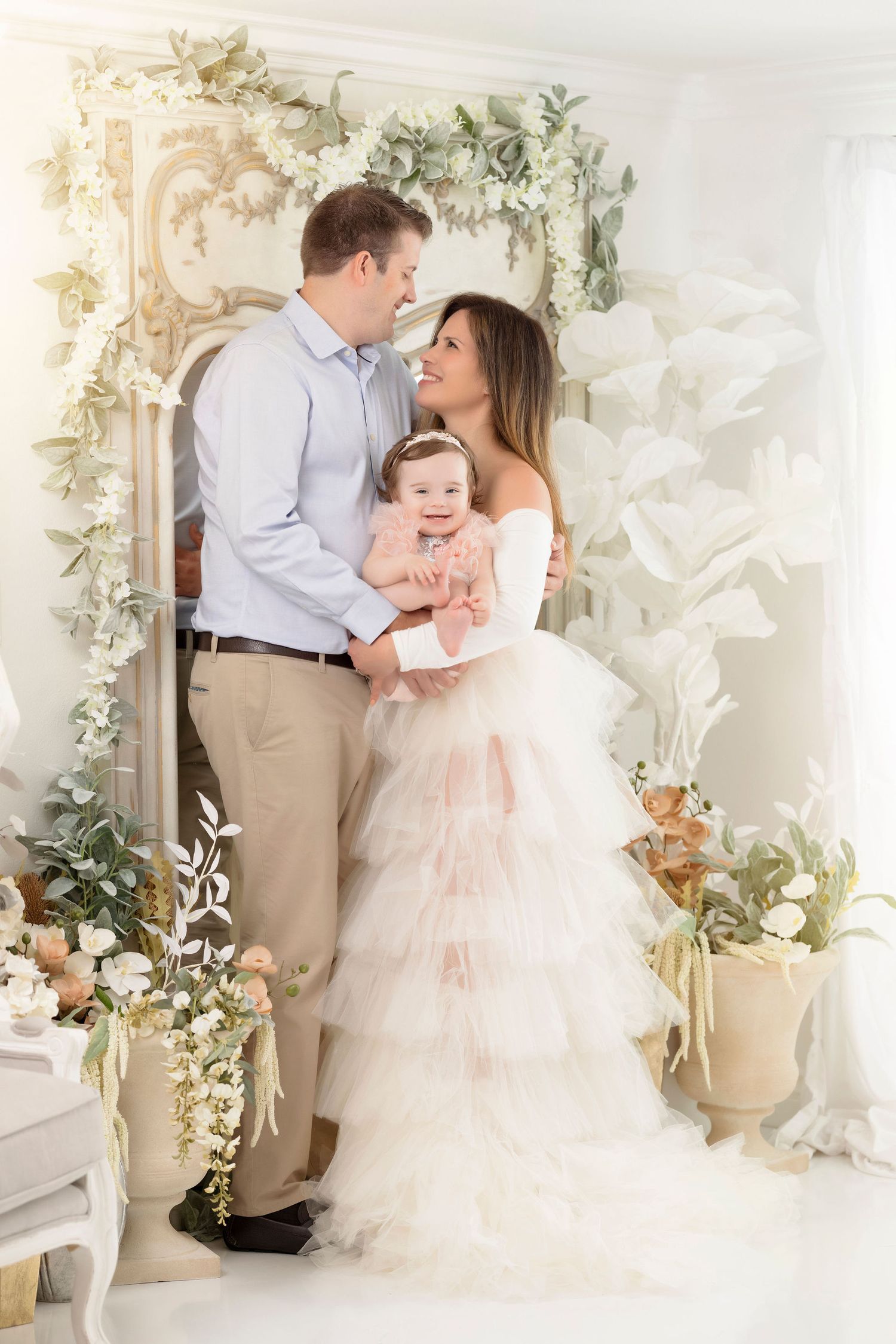 Romantic family moment in white studio with floral arch and greenery.