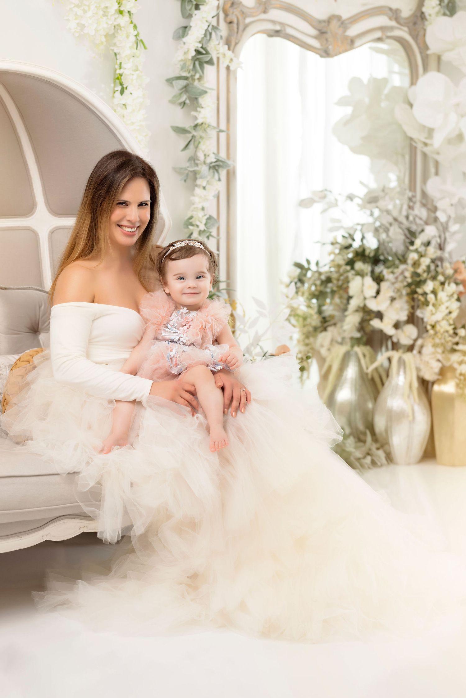 An ethereal portrait in white featuring a flowing tulle gown and elegant floral decorations in a light-filled studio setting.