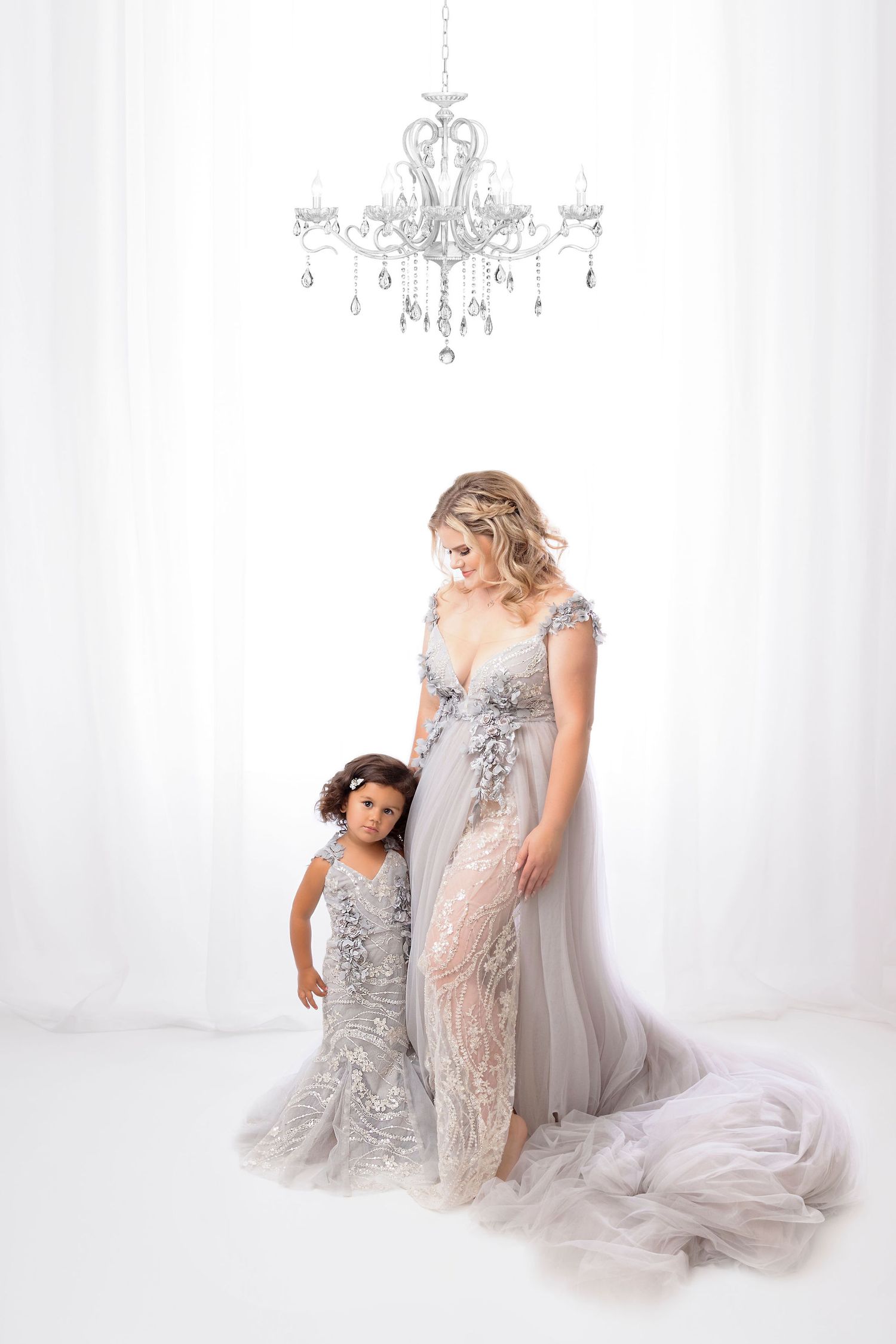 Studio portrait under crystal chandelier featuring matching grey lace dresses.