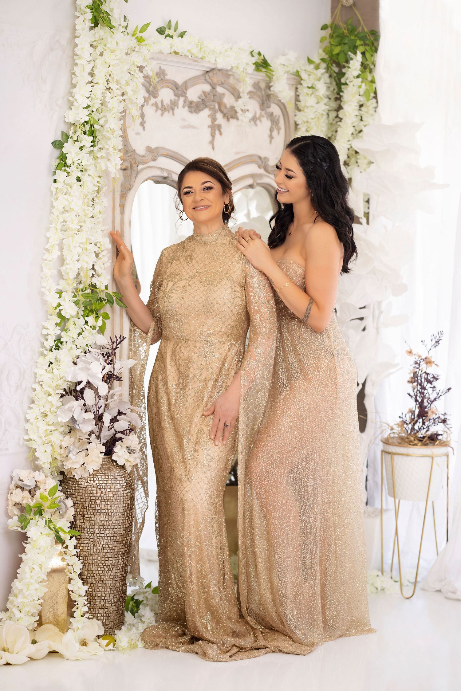 Elegant portrait with gold dresses against white floral archway and decor.