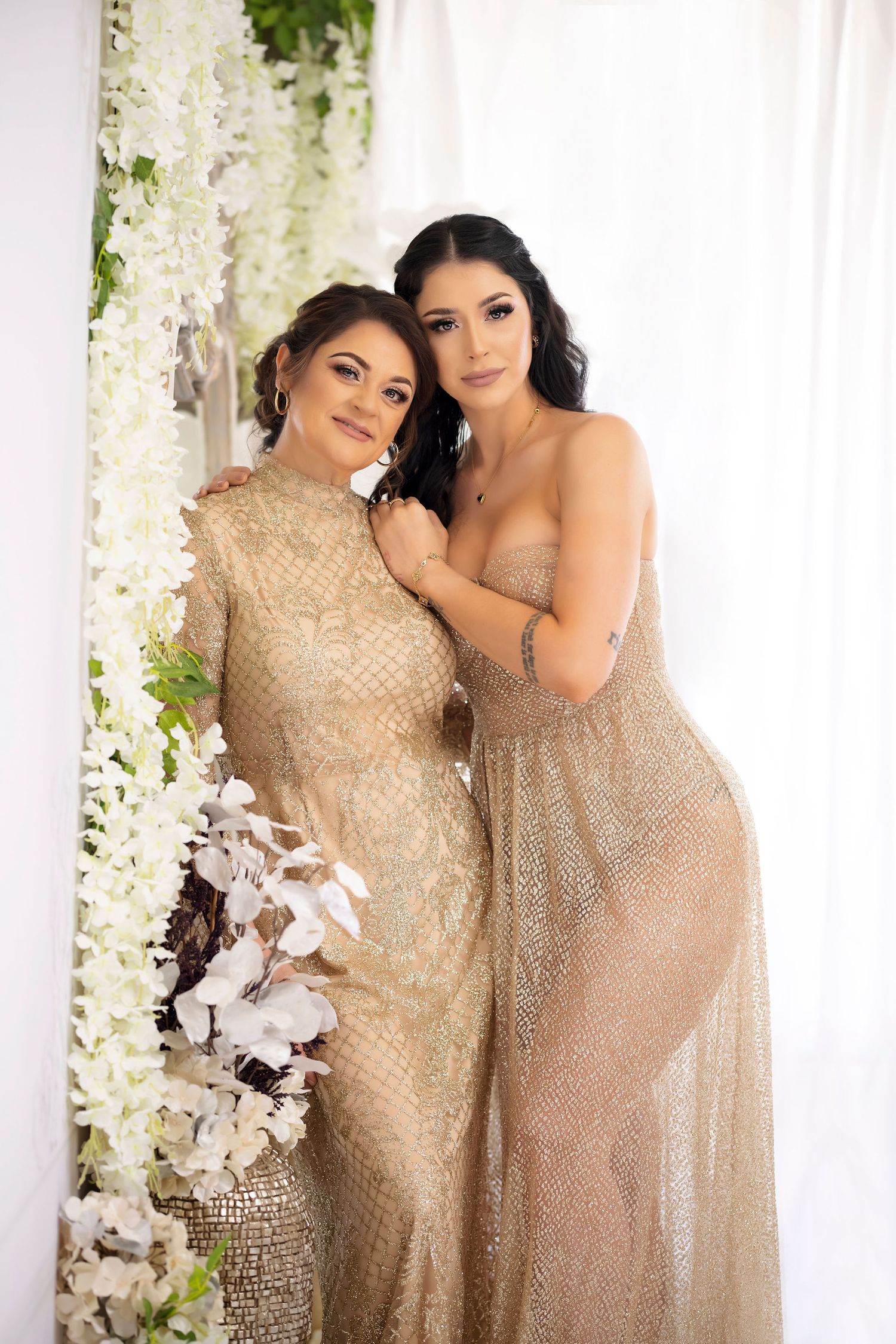 Glamorous studio portrait featuring sheer champagne gowns against floral backdrop.