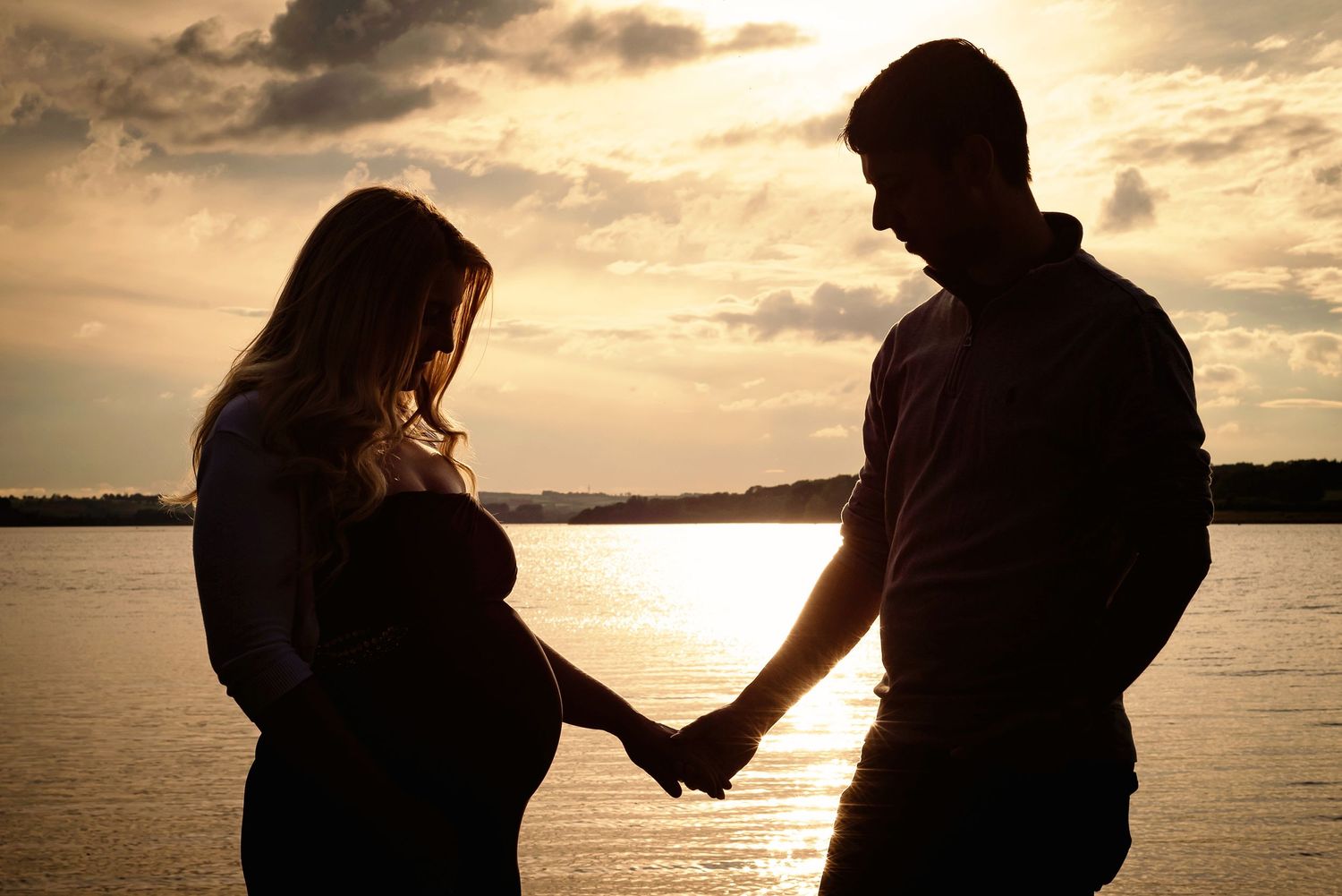 Silhouetted couple holding hands at sunset by a peaceful lake.