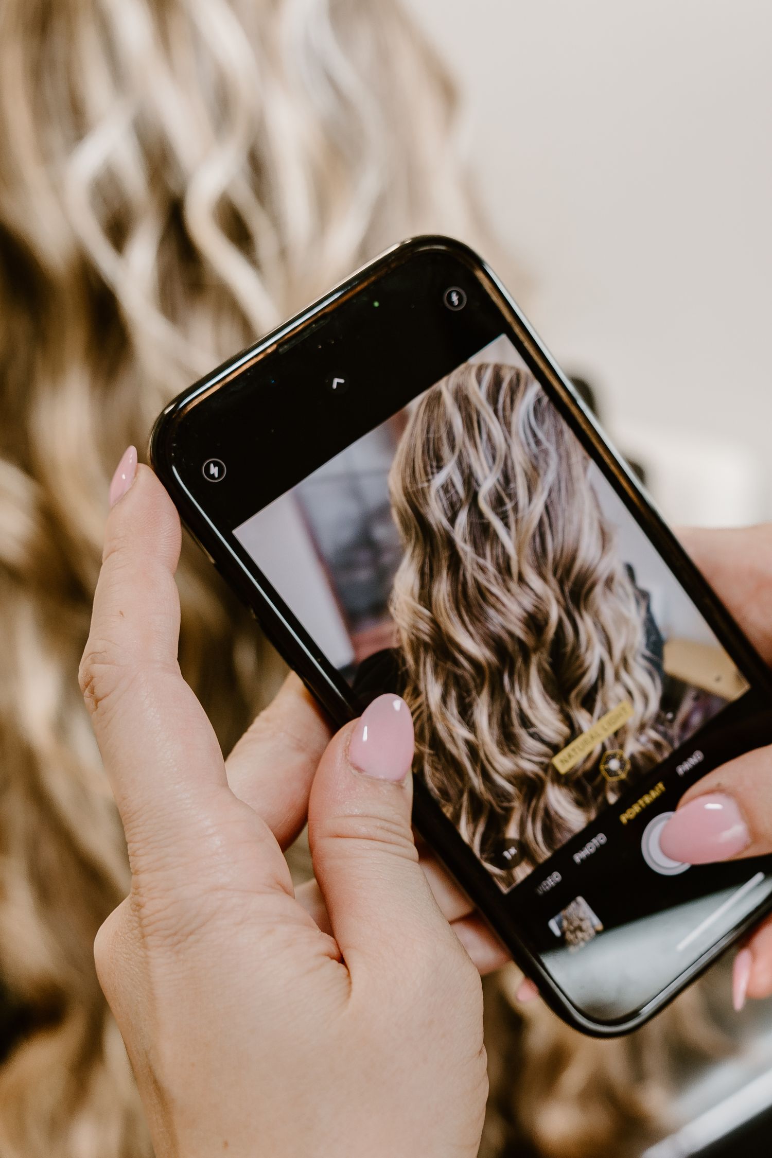 Phone capturing photo of freshly styled wavy blonde hair in salon mirror.