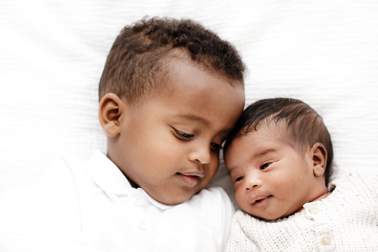 Two babies lying together peacefully on white bedding in a heartwarming close-up portrait.