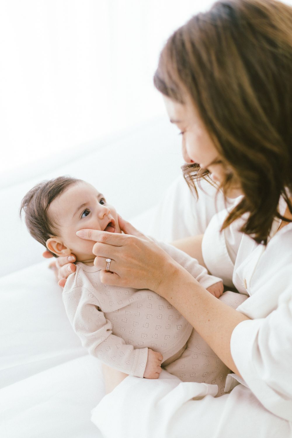 Parent cradling baby's face during intimate moment on white bedding.