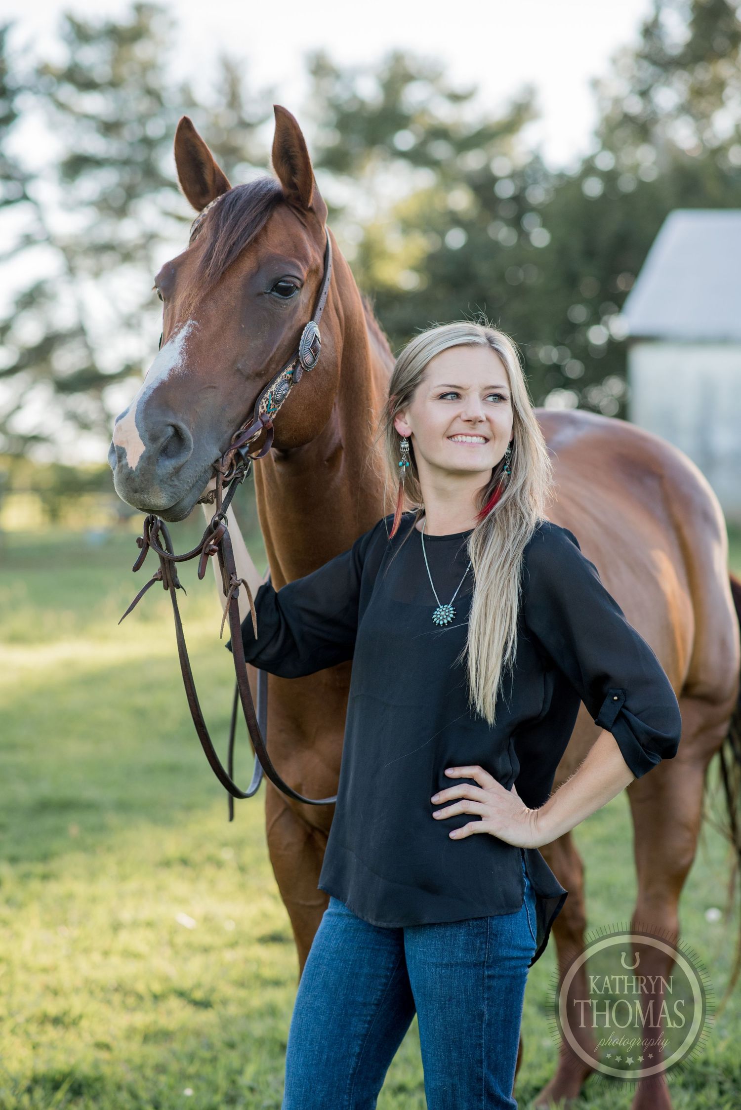 A beautiful chestnut horse with bridle poses with its handler against a natural backdrop.