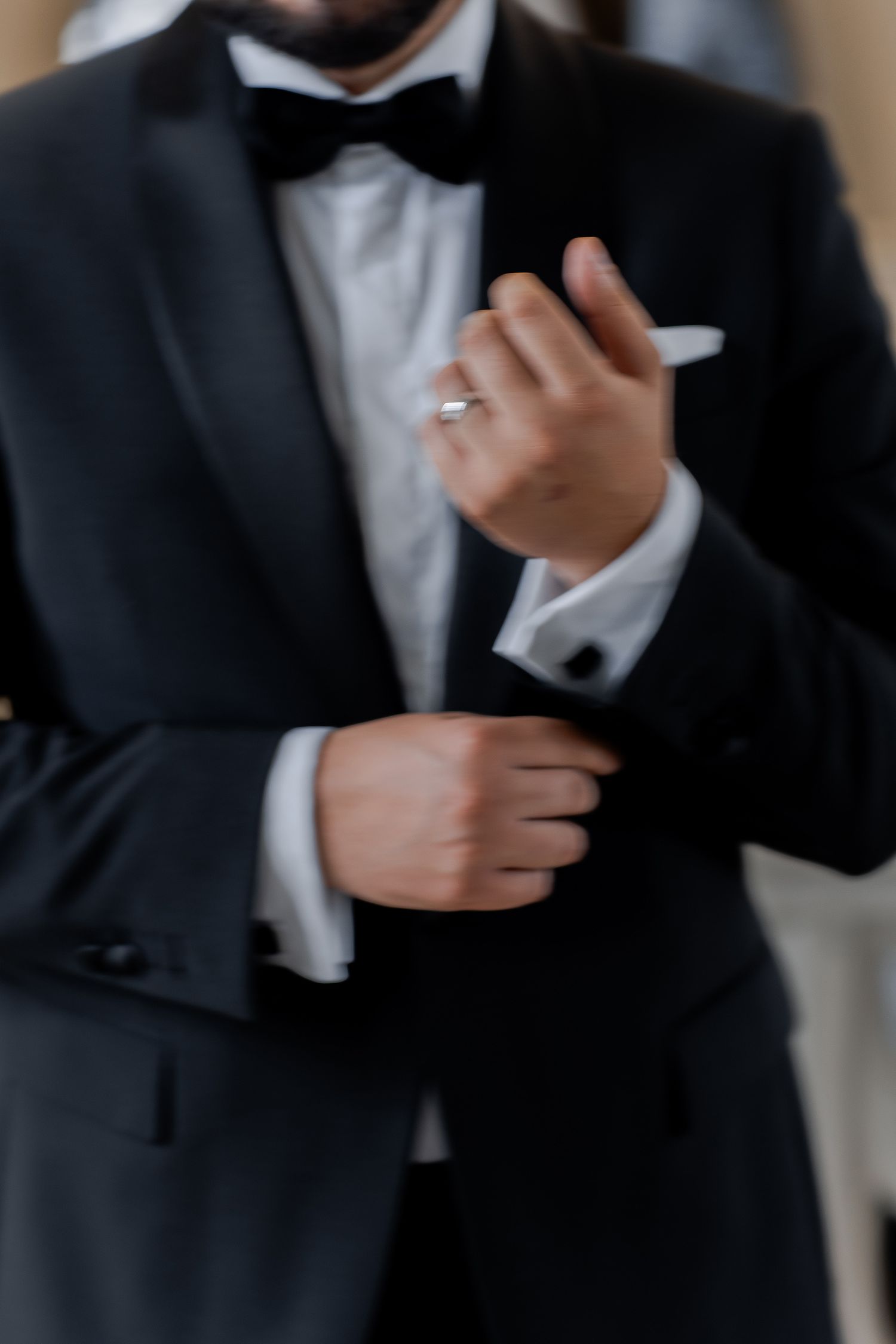 Close-up detail of groom adjusting formal wear and wedding ring.