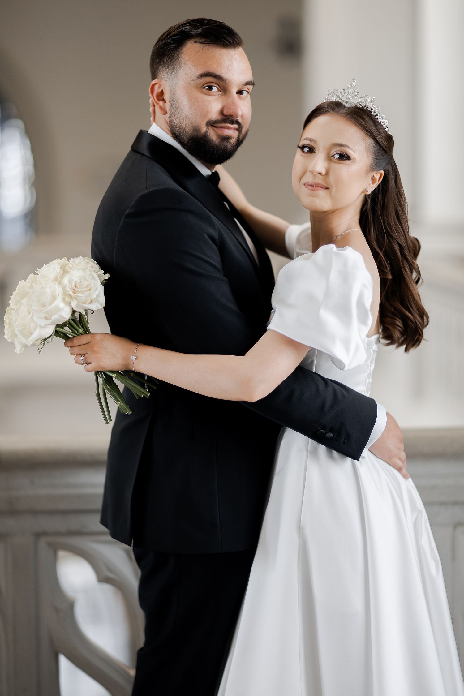 Elegant wedding portrait of couple with white bouquet in classical architectural setting.