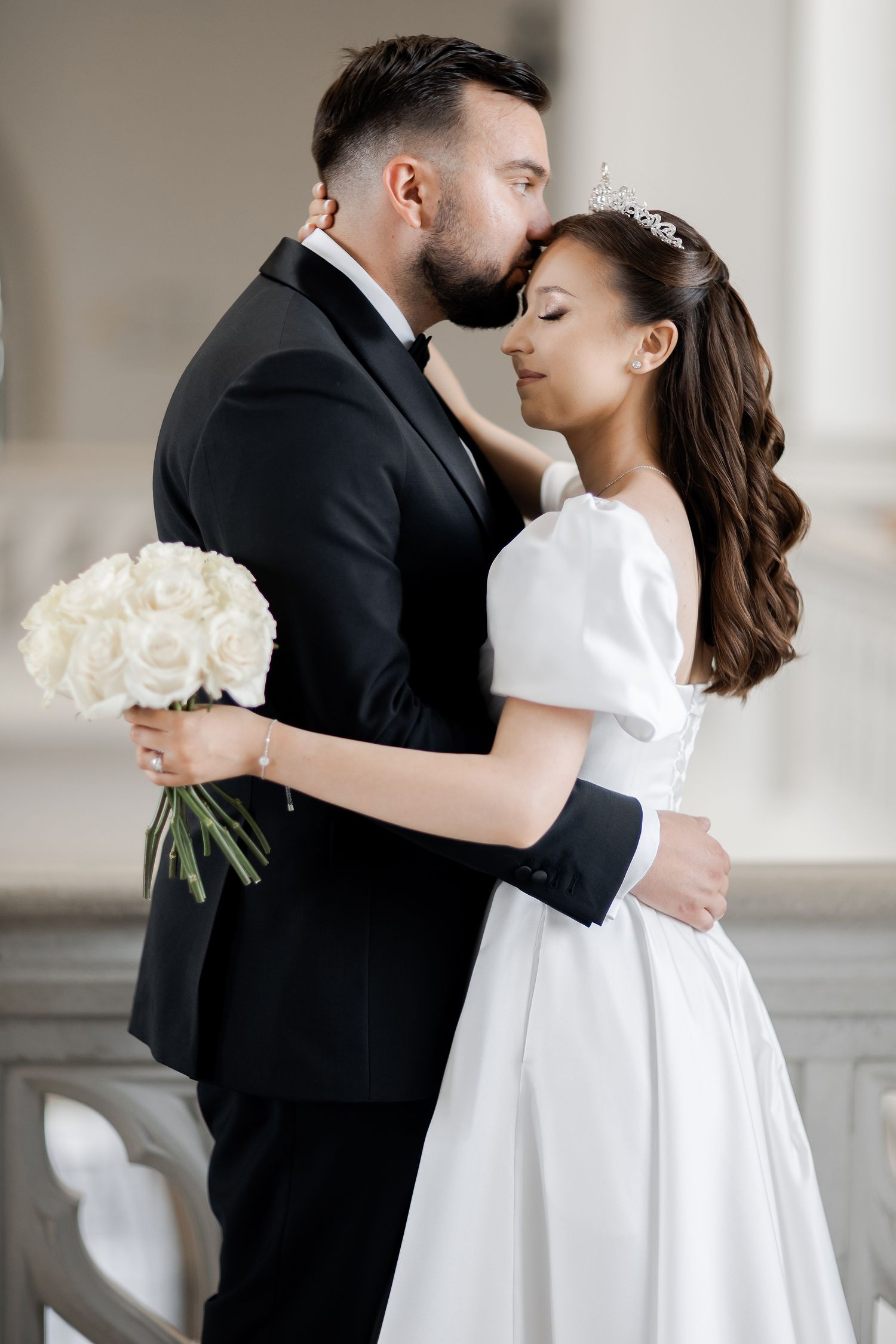 A romantic wedding photo showing a couple embracing, with the bride holding a white bouquet of flowers.