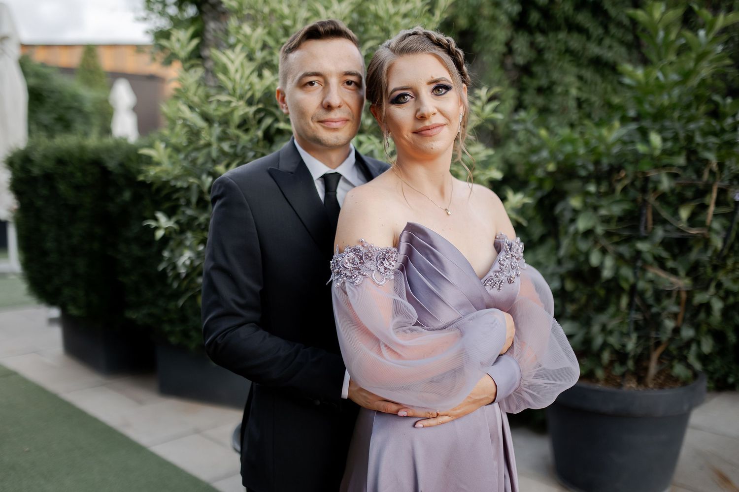 A formal couple's portrait in an outdoor garden setting with lavender dress and black suit.