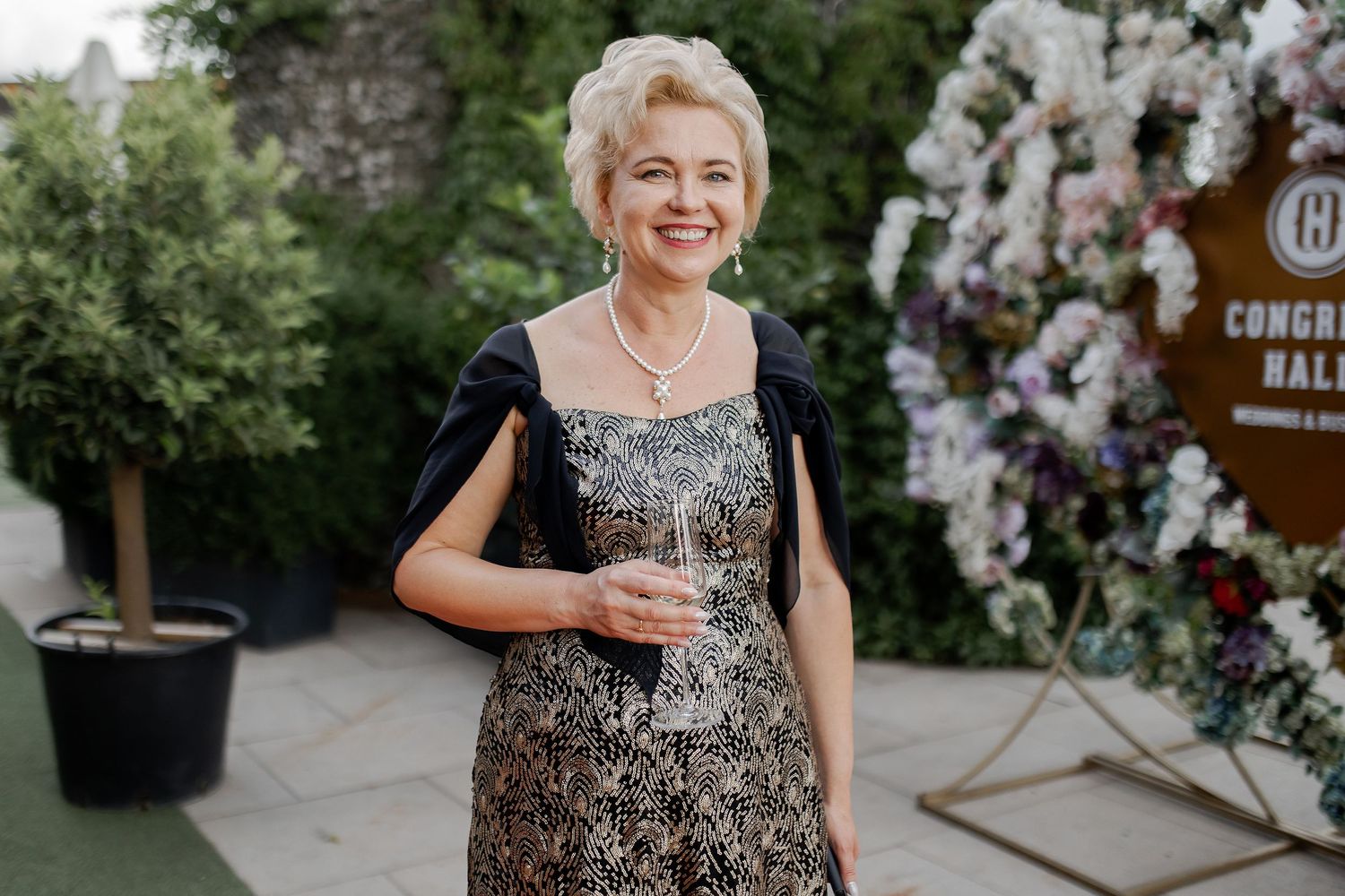 An elegant woman in a sparkly black and gold dress poses at an outdoor event.