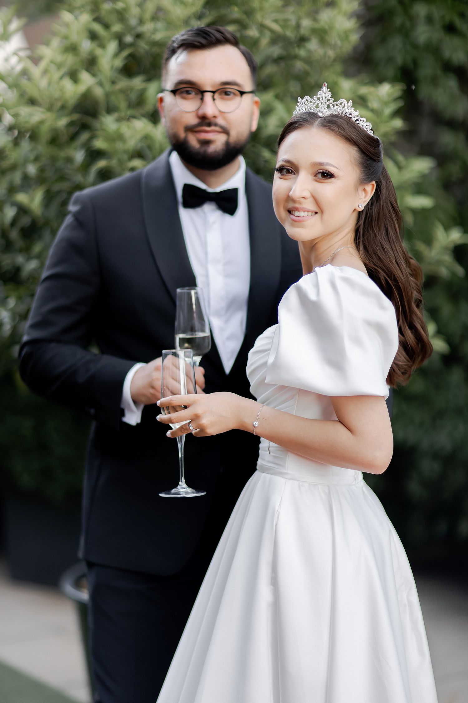 A joyful wedding couple shares a celebratory moment with champagne in an outdoor setting.