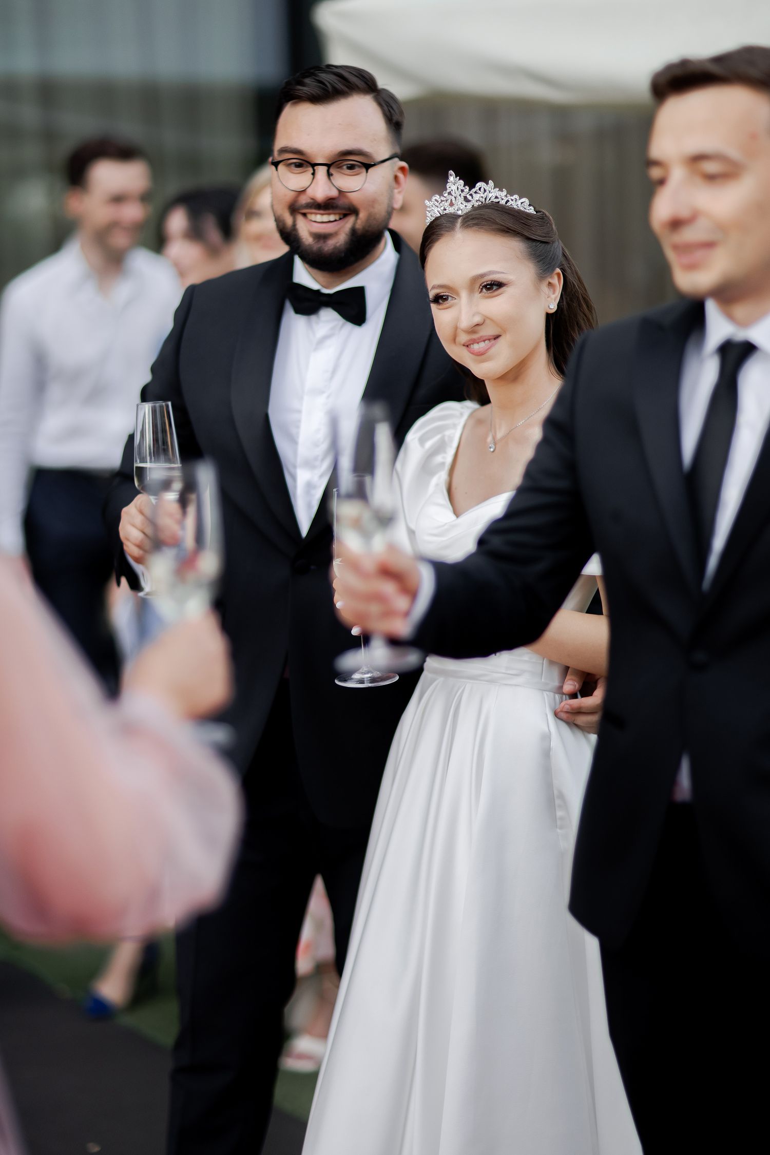 Wedding party guests in formal attire gather for champagne toast at outdoor celebration.