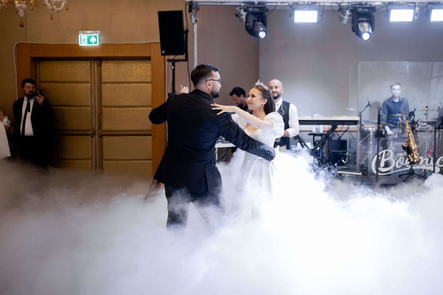 Couple dances surrounded by dramatic fog effects at indoor wedding reception.