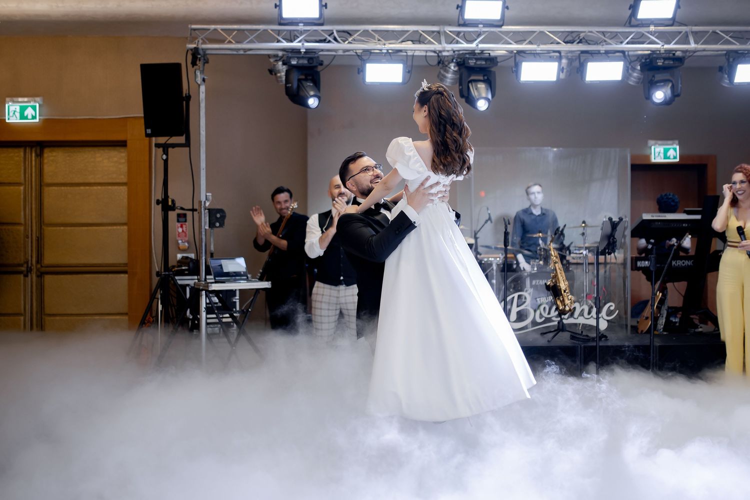 Wedding couple performs elegant dance lift through atmospheric fog on dance floor.